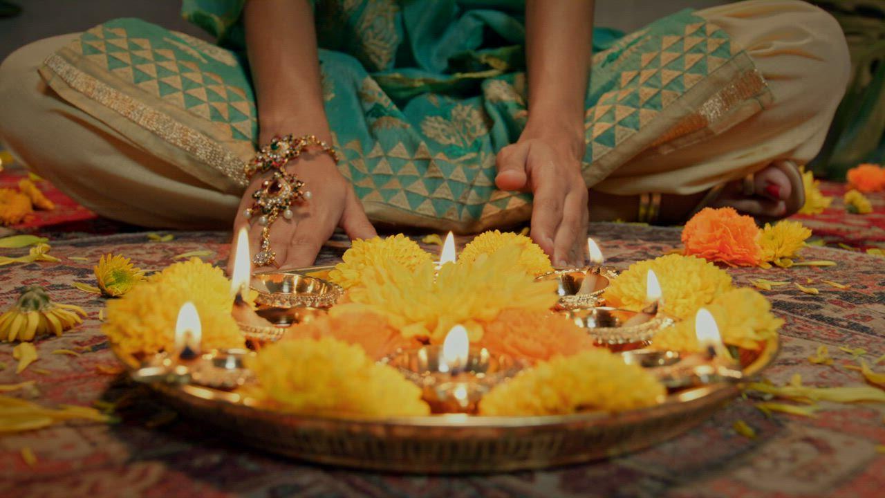 Hands lifting a Diwali offering with burning diyas
